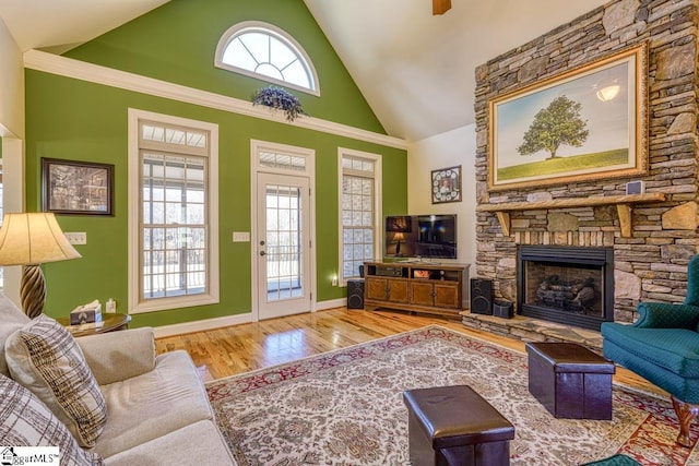 living room with high vaulted ceiling, wood-type flooring, a stone fireplace, and a healthy amount of sunlight