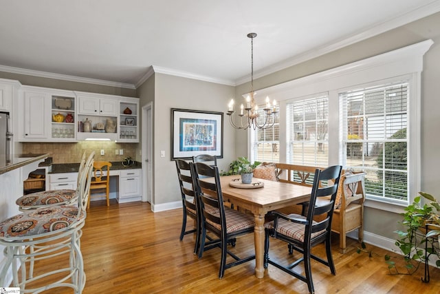 dining room with built in desk, a chandelier, light hardwood / wood-style flooring, and crown molding