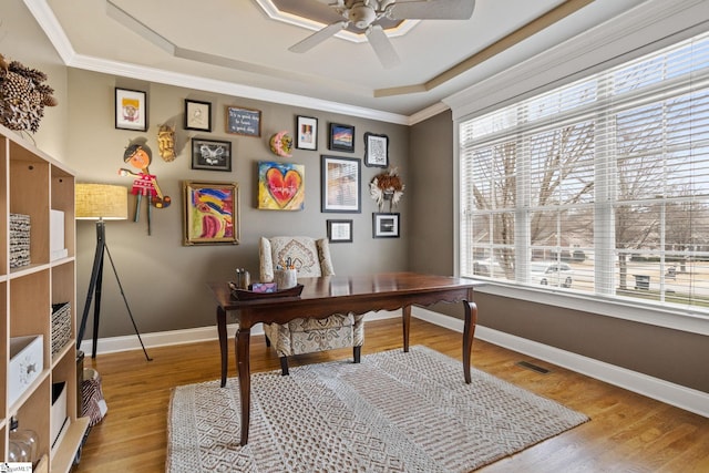 home office with ceiling fan, ornamental molding, light hardwood / wood-style floors, and a tray ceiling