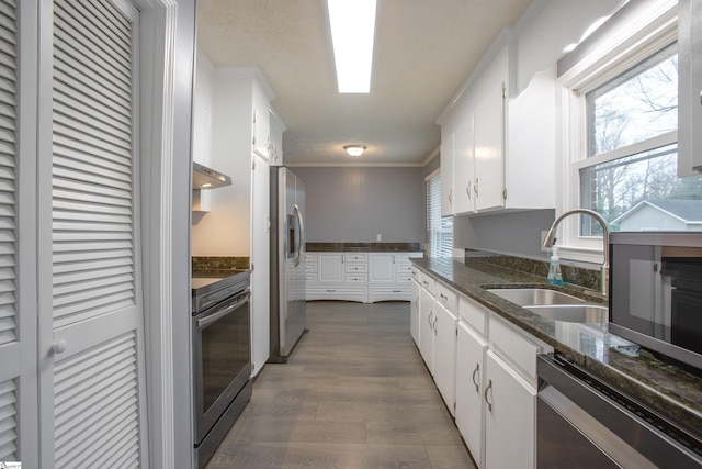 kitchen featuring white cabinets, stainless steel appliances, dark stone counters, sink, and crown molding