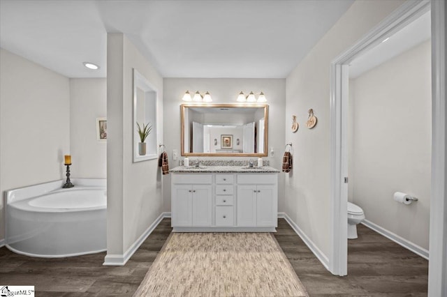 bathroom featuring hardwood / wood-style floors, toilet, a tub to relax in, and vanity