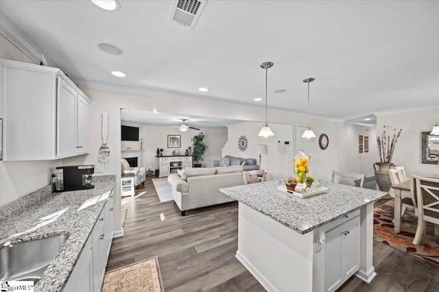 kitchen with pendant lighting, white cabinets, a kitchen island, wood-type flooring, and sink