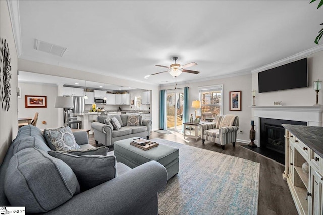 living room featuring ceiling fan, dark wood-type flooring, and crown molding