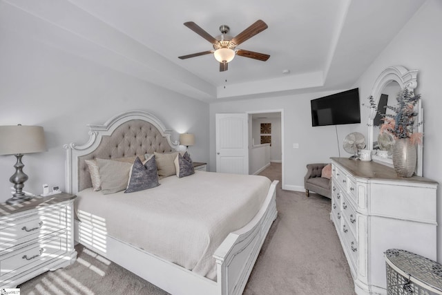 carpeted bedroom with ceiling fan and a tray ceiling