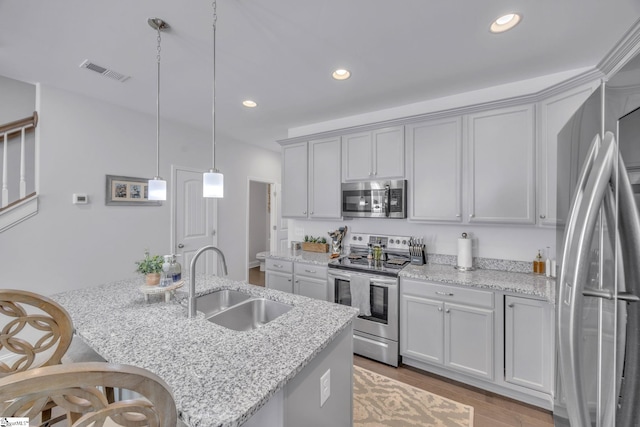 kitchen featuring sink, stainless steel appliances, light stone counters, and a kitchen island with sink