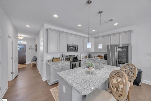 kitchen featuring appliances with stainless steel finishes, decorative light fixtures, a kitchen island with sink, light stone counters, and a breakfast bar area