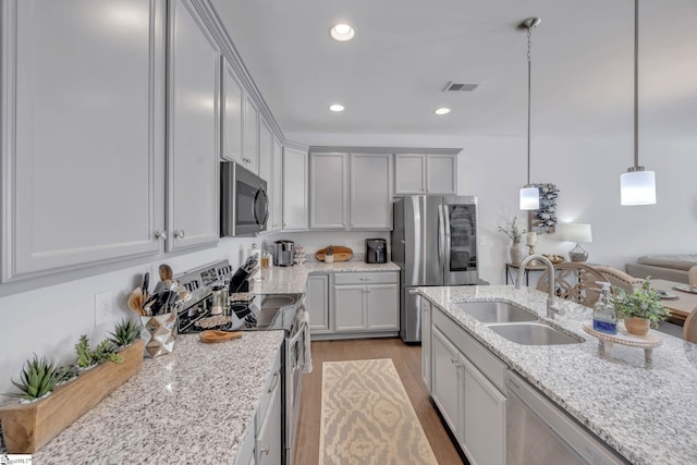 kitchen with appliances with stainless steel finishes, sink, hanging light fixtures, light wood-type flooring, and light stone counters