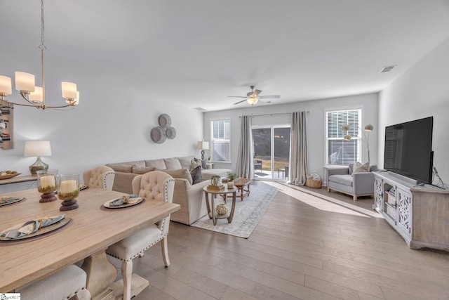 living room featuring ceiling fan with notable chandelier and light wood-type flooring