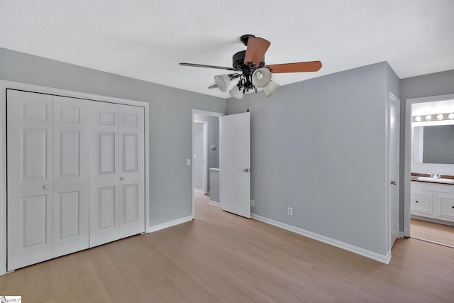 unfurnished bedroom featuring ceiling fan, sink, light wood-type flooring, ensuite bath, and a closet