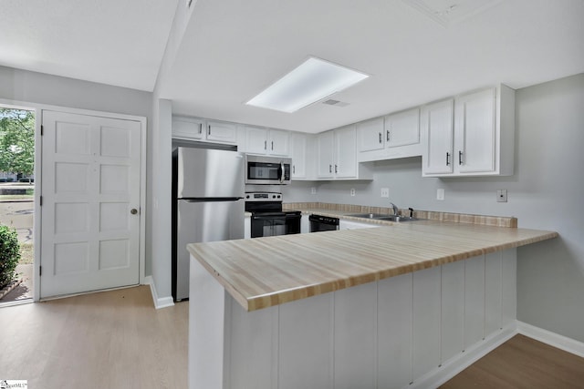 kitchen with appliances with stainless steel finishes, white cabinetry, light hardwood / wood-style floors, sink, and kitchen peninsula