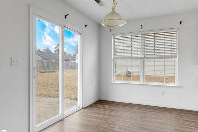 unfurnished dining area featuring plenty of natural light, a textured ceiling, and light wood-type flooring