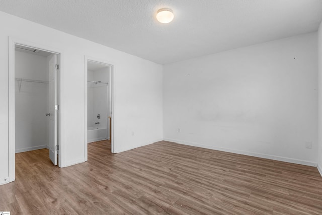 unfurnished bedroom with a textured ceiling, light hardwood / wood-style flooring, a closet, and a walk in closet