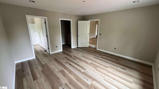 unfurnished bedroom featuring wood finished floors, a spacious closet, a closet, and baseboards