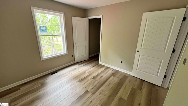 unfurnished bedroom with baseboards, light wood finished floors, and multiple windows