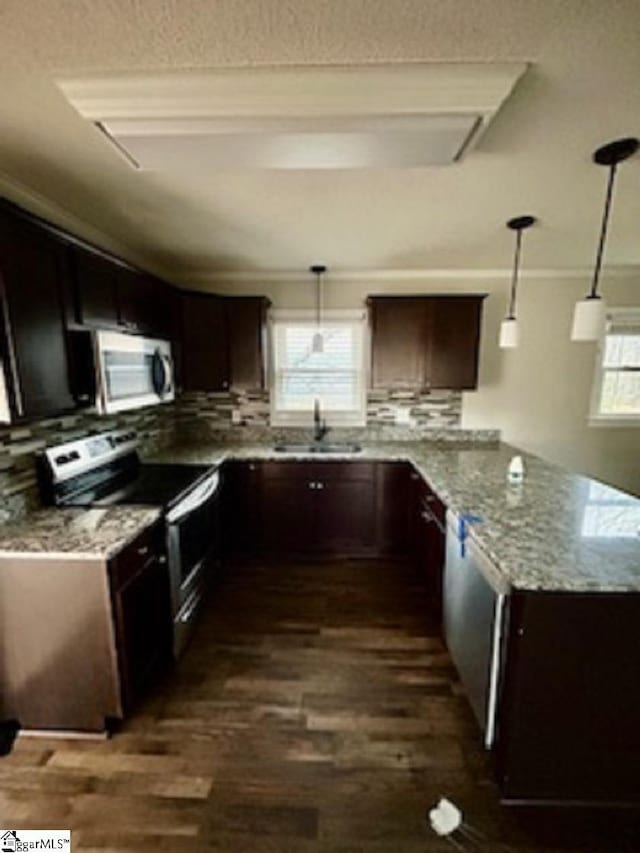 kitchen with appliances with stainless steel finishes, sink, dark brown cabinets, pendant lighting, and light stone counters