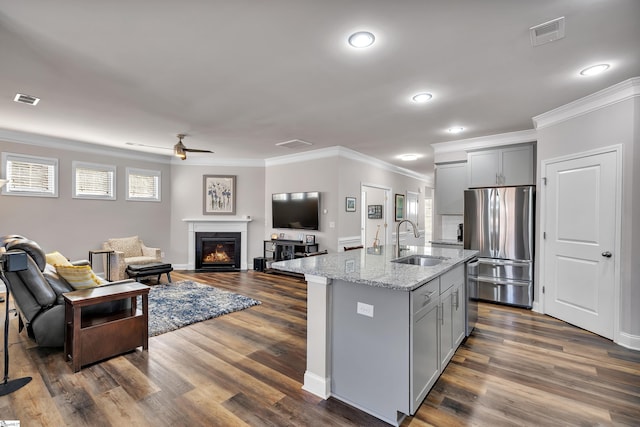 kitchen featuring gray cabinetry, sink, stainless steel fridge, light stone counters, and a center island with sink