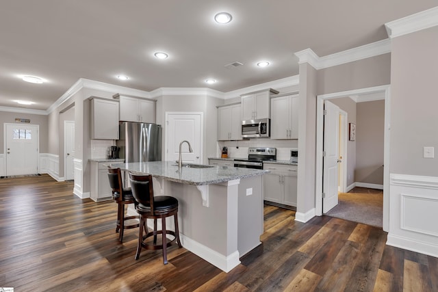 kitchen with appliances with stainless steel finishes, sink, light stone counters, gray cabinets, and a kitchen island with sink