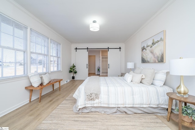 bedroom with light wood-type flooring, a barn door, and crown molding