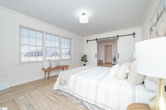 bedroom with light hardwood / wood-style flooring, a barn door, and crown molding