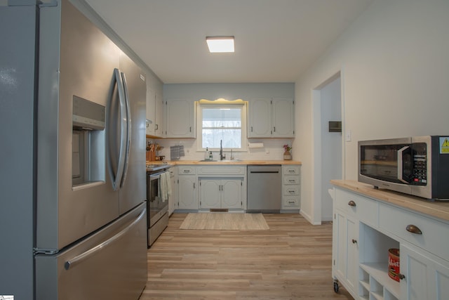 kitchen with light hardwood / wood-style floors, appliances with stainless steel finishes, decorative backsplash, white cabinets, and sink