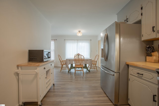 kitchen with stainless steel refrigerator with ice dispenser, white cabinets, light wood-type flooring, and wooden counters