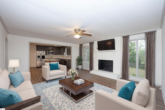 living room with ceiling fan, sink, light hardwood / wood-style flooring, and a brick fireplace