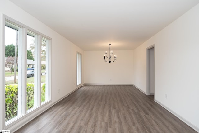 empty room with a chandelier, plenty of natural light, and dark wood-type flooring