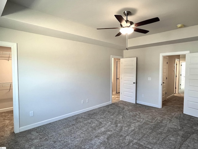 unfurnished bedroom featuring a closet, ceiling fan, dark carpet, and a spacious closet