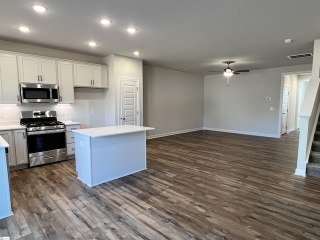 kitchen with ceiling fan, appliances with stainless steel finishes, white cabinetry, dark hardwood / wood-style floors, and a kitchen island