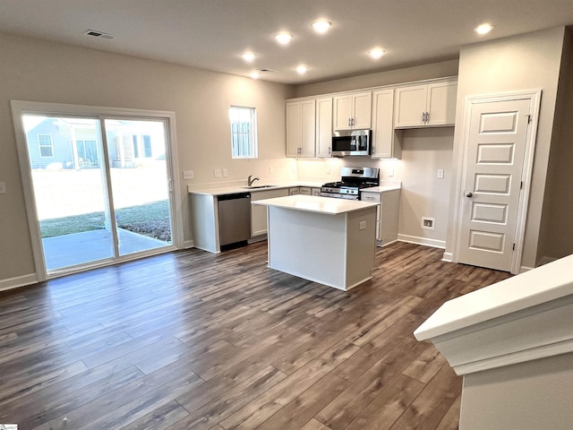 kitchen with a center island, appliances with stainless steel finishes, white cabinetry, sink, and dark hardwood / wood-style floors