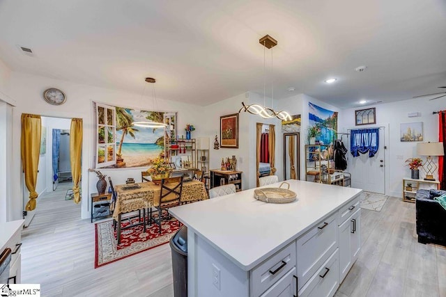 kitchen with light wood-type flooring, decorative light fixtures, a center island, and white cabinetry