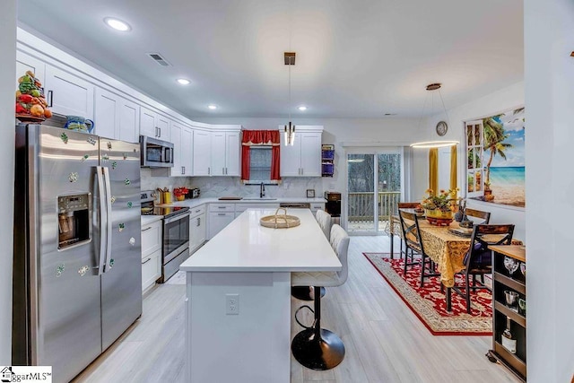 kitchen with a center island, decorative light fixtures, white cabinetry, and appliances with stainless steel finishes