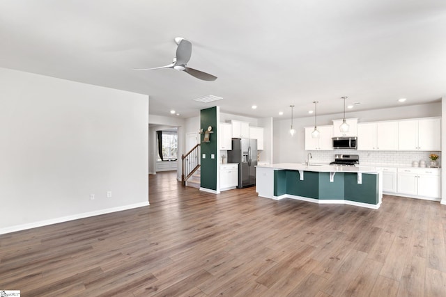 kitchen featuring appliances with stainless steel finishes, decorative light fixtures, white cabinetry, an island with sink, and sink