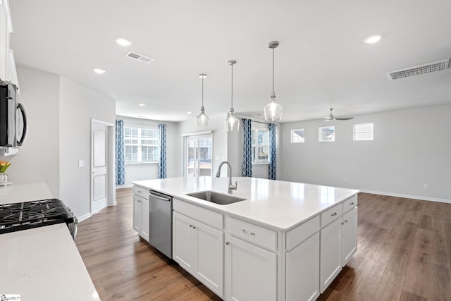 kitchen featuring dishwasher, sink, decorative light fixtures, white cabinets, and a center island with sink