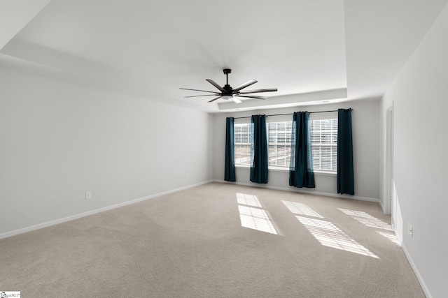 empty room with ceiling fan, a raised ceiling, and light carpet