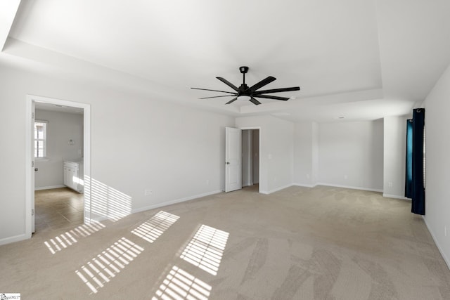 empty room featuring ceiling fan, light colored carpet, and a tray ceiling