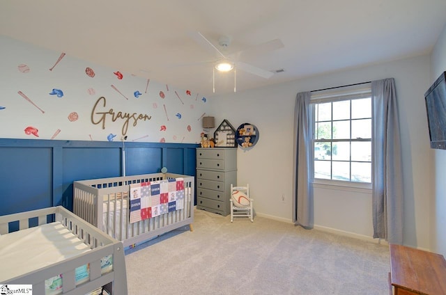 bedroom with ceiling fan, light colored carpet, and a crib