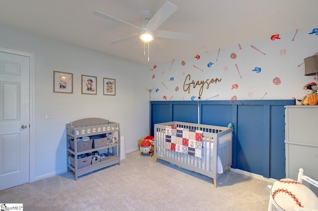 carpeted bedroom featuring ceiling fan and a nursery area