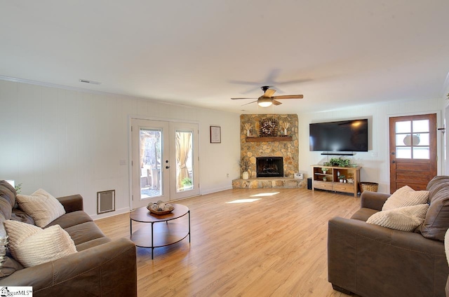 living room featuring ceiling fan, french doors, light hardwood / wood-style flooring, and a stone fireplace