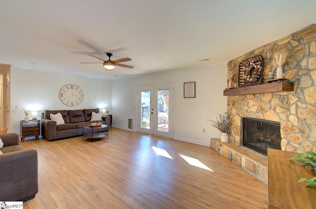 living room featuring crown molding, ceiling fan, french doors, a stone fireplace, and light hardwood / wood-style floors