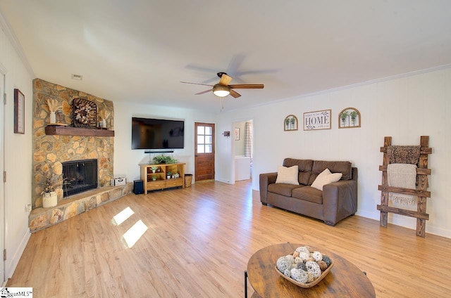 living room featuring ceiling fan, light wood-type flooring, a stone fireplace, and ornamental molding