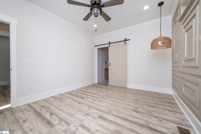 unfurnished bedroom with light wood-type flooring, ceiling fan, a barn door, and crown molding