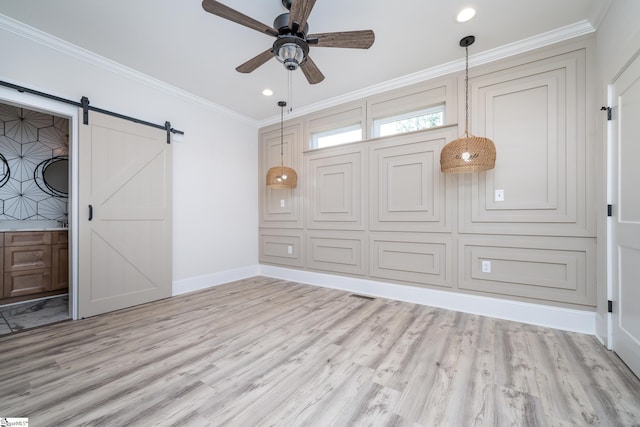 interior space featuring ceiling fan, light hardwood / wood-style flooring, a barn door, and ornamental molding