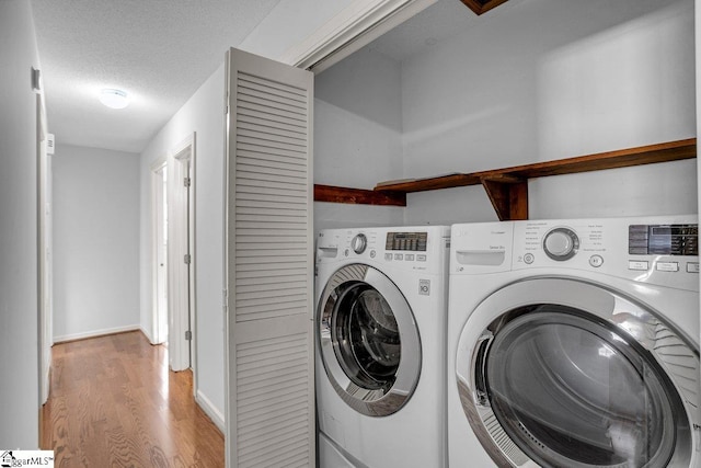 laundry room featuring light hardwood / wood-style floors, a textured ceiling, and washing machine and clothes dryer