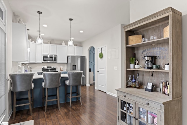 kitchen featuring pendant lighting, appliances with stainless steel finishes, a kitchen bar, white cabinetry, and dark hardwood / wood-style floors