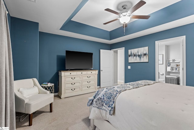 bedroom with ceiling fan, light colored carpet, connected bathroom, and a raised ceiling