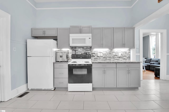 kitchen featuring white appliances, a towering ceiling, tasteful backsplash, light tile patterned flooring, and gray cabinetry