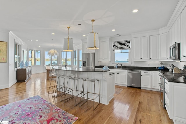 kitchen with pendant lighting, white cabinets, ornamental molding, a kitchen island, and stainless steel appliances