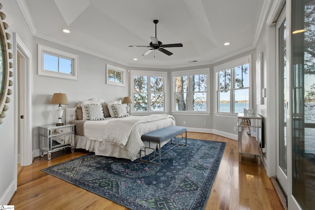 bedroom with ceiling fan, wood-type flooring, a tray ceiling, and a water view