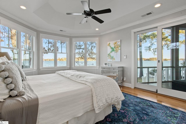 bedroom with wood-type flooring, a water view, a raised ceiling, access to outside, and ceiling fan